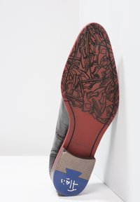 Scarpa di pelle nera con una suola a motivo rosso e nero. Presenta un tacco grigio e un accento blu sul retro con un logo. Texture liscia.