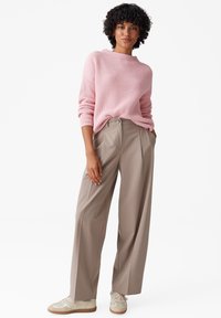 Felpa a coste rosa chiaro, vestibilità ampia; pantaloni beige a vita alta con gamba larga e dettagli plissettati; sneakers crema con dettagli rosa chiaro.