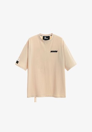 Camiseta beige de manga corta oversize con cuello redondo, logo negro "MWM" en el pecho, etiqueta dentro del cuello y pequeña etiqueta en la manga izquierda.