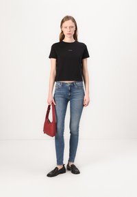 Tricou scurt negru cu un logo, blugi skinny albaștri, mocasini negri și o geantă roșie de umăr. Material fin și design ajustat.