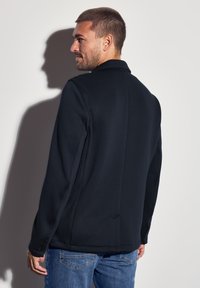 Marineblazer mit Reverskragen und einem Knopfverschluss, ausgestattet mit einer glatten Textur und taillierter Passform, kombiniert mit blauen Jeans.