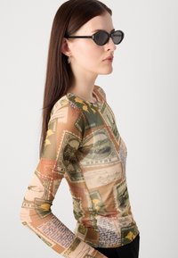 Long-sleeve top made of lightweight fabric featuring a postage stamp print in earthy tones. Round neckline and fitted shape. Black sunglasses worn.
