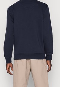 Tmavě modrá mikina s dlouhými rukávy, kulatým výstřihem a žebrovanými manžetami a lemem; vyrobená z měkké látky s hladkou texturou a minimalistickým designem.