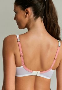 Reggiseno in tessuto bianco con una tracolla regolabile rosa. Tra le caratteristiche notevoli ci sono la chiusura a gancio e una delicata stampa floreale sui bordi delle tracolle.