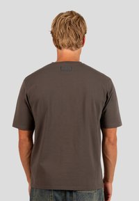 Tmavě šedé tričko s krátkým rukávem a kulatým výstřihem, na zadní straně s texturovanou nášivkou loga. Materiál z bavlny s hladkým povrchem.