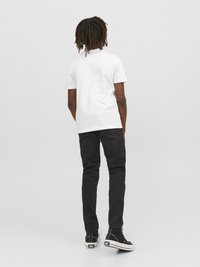 Camiseta blanca de algodón con mangas cortas, combinada con jeans ajustados negros y zapatillas altas negras. Diseño simple, sin patrones visibles.
