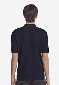 Marinblå kortärmad polotröja med en strukturerad stickad design, med en klassisk krage och ribbade ärmslut. Vy bakifrån.