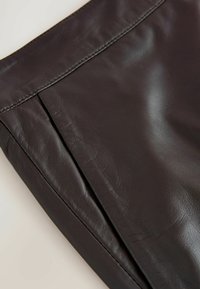 Tessuto in pelle nera con una superficie liscia, caratterizzato da un dettaglio a plissé verticale e una cucitura pulita lungo la vita.