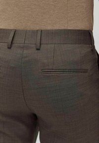 Brązowe spodnie o dopasowanym kroju, wyróżniające się teksturowaną tkaniną, slim fit, bocznymi kieszeniami oraz dyskretną tylną kieszenią z wąskim otworem.