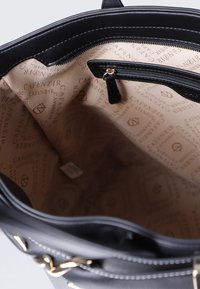 Svart läderhandväska med guldfärgad detalj, med en zippered ficka och en beige inredning klädd med ett upprepande logomönster.