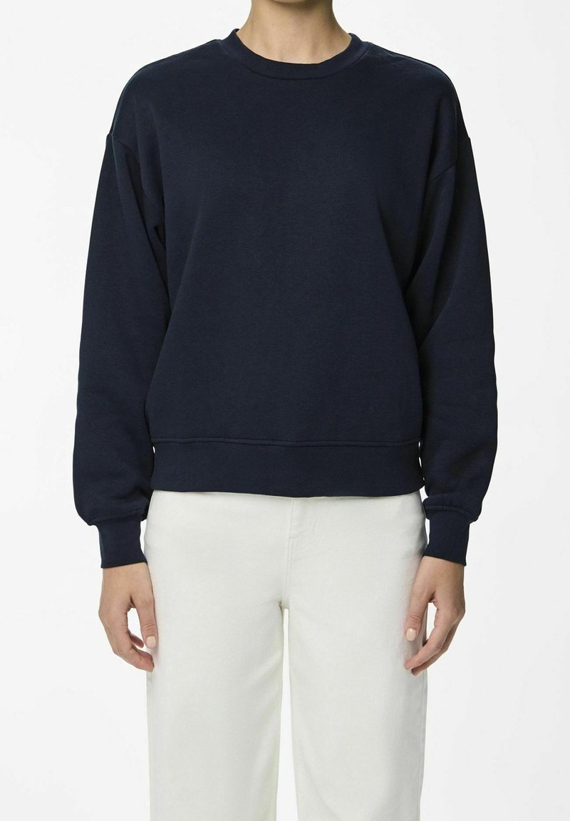 Marinblå sweatshirt i mjukt tyg, med rund halsringning, sänkta axlar och ribbade ärmslut. Bärs över ljusbeiga byxor.