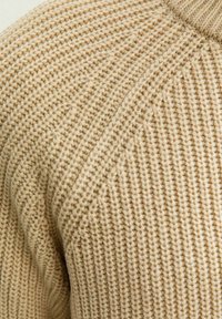 Beżowy sweter wykonany na drutach z teksturowanej włóczki, z prążkowanymi detalami wzdłuż dekoltu oraz diagonalnym wzorem dzianiny na całym ciele.