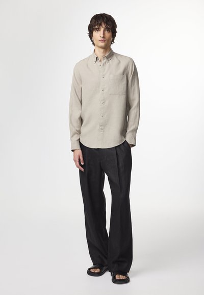 Light beige linen shirt with a collar and single chest pocket, paired with black wide-leg trousers and black sandals. Smooth texture.