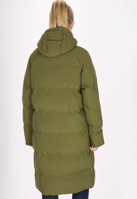 Olivgrön vadderad kappa med huva, med vertikala quiltade sektioner och långa ärmar, som når till halva vaden. Mjuk, jämn textur.