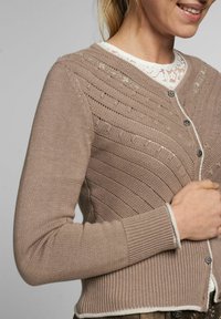 Beige gestrickte Strickjacke mit einem strukturierten Wellenmuster, Rundhals, silbernen Knöpfen und kontrastierendem weißen Saum an den Ärmelenden und am Bund.