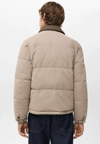 Beżowa puchowa kurtka z pikowanym wzorem, brązowym kołnierzem i zapinanymi na guziki mankietami. Materiał wydaje się miękki i lekki.