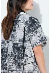 Top bianco e nero a maniche corte con stampa di giornale, caratterizzato da una vestibilità rilassata e da un dettaglio con cordino a contrasto sul lato.
