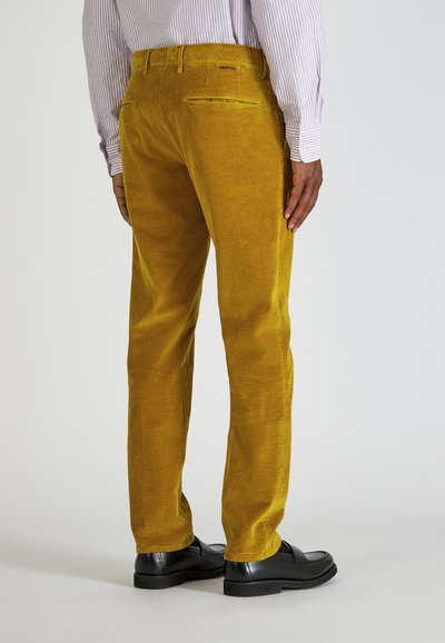 Gele corduroy broek met een gestructureerde afwerking, voorzien van achterzakken en een rechte pijp, gecombineerd met zwarte schoenen.