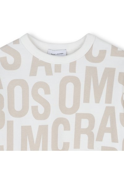T-shirt blanc à col rond avec de grandes lettres beige dispersées au hasard ; étiquette Marc Jacobs visible à l'intérieur du col.