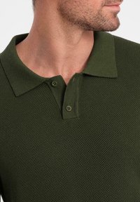 Mörkgrön stickad polo med klassisk krage, tvåknapps knappslå och textilstruktur med ett subtilt mönster.