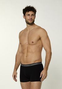 Czarne bokserki męskie z szarą elastyczną gumą w pasie z napisem "nur die." Gładka tkanina i dopasowany krój zwiększają komfort.