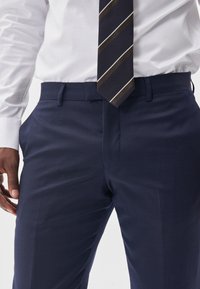 Marinblå klänningsbyxor i mjukt tyg med en åtsittande design, utrustade med sidofickor och en slät front, kompletterade med en randig slips.