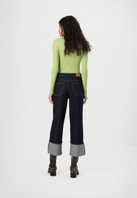 Top de manga larga verde de canalé ajustado, combinado con unos jeans de pierna ancha de mezclilla oscura con puños doblados y una etiqueta de cuero en la parte trasera de la cintura.