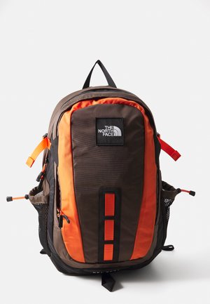 Mochila The North Face em castanho escuro e laranja, com bolsos frontais e laterais, alças ajustáveis e uma pega na parte superior.