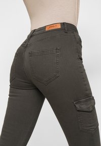 Jeans skinny verde oscuro con un acabado texturizado, que cuentan con una etiqueta de parche en la cintura y dos bolsillos traseros con solapas angulares.