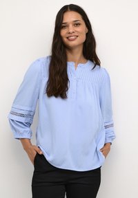 Blusa azzurro chiaro, con texture, dal collo rotondo, chiusura a bottone e maniche a tre quarti con dettagli in pizzo.