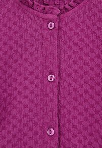 Vijolični kardigan z teksturo in vzorčasto površino, ki ima naborkan ovratnik in pet usklajenih gumbov spredaj.