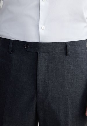 Biała koszula na guziki wpuszczona w ciemnoszare, dopasowane spodnie z przodu z guzikiem i szlufkami, przedstawiona od talii do połowy uda.