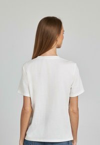 Maglietta bianca in cotone con scollo tondo e maniche corte, caratterizzata da un design semplice e da una texture morbida, mostrata da dietro.