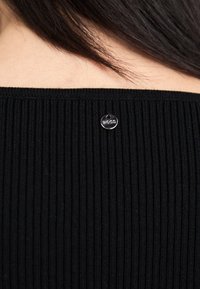 Črn rebrast materialni top s dizajnom brez naramnic, ki vsebuje srebrno nalepko z vgraviranim napisom "BOSS". Gladka tekstura in oprijet kroj.