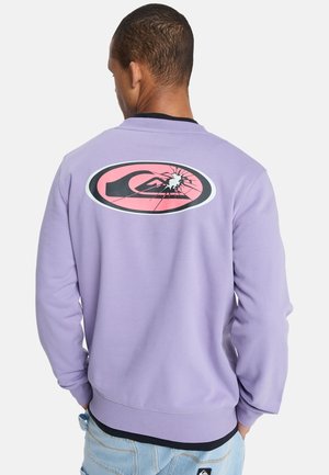 Paarse trui met een ronde afbeelding op de achterkant met een roze en zwarte tekening. Geribbelde manchetten en zoom, zachte stoftextuur.