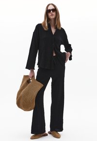 Černá texturovaná blůza spolu s odpovídajícími širokými kalhotami, doplněná tkanou hnědou taškou a nazouvacími botami s leopardím potiskem.