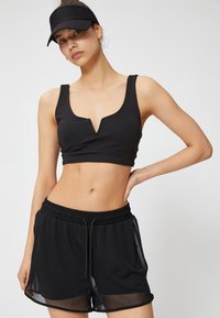 Top deportivo negro cortado con cuello en V y tirantes anchos, combinado con pantalones cortos negros holgados que cuentan con una cinturilla elástica y acentos transparentes.