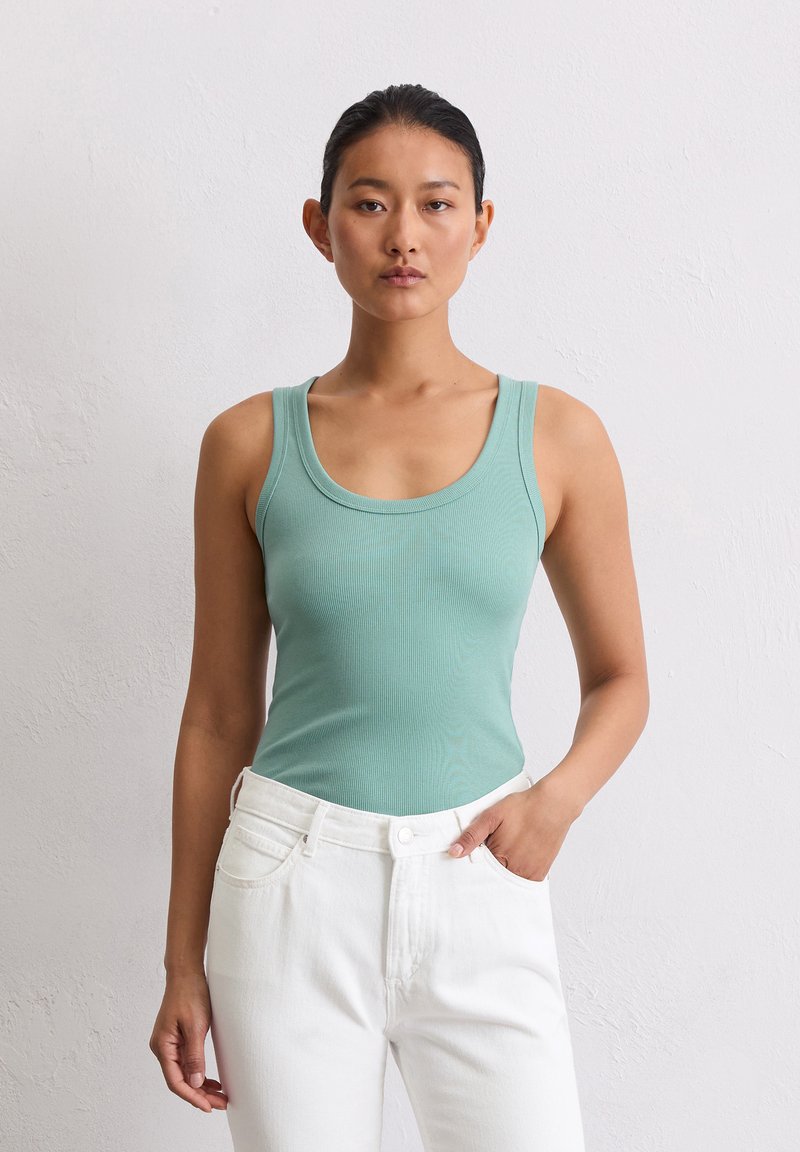 Un débardeur côtelé en bleu clair avec un col rond, associé à un jean en denim blanc taille haute. Le tissu est doux et ajusté.