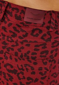 Červená kordurová látka s čiernym leopardím vzorom. Obsahuje malú nálepku s nápisom "vytvorte sa sami" a detaily stehov.