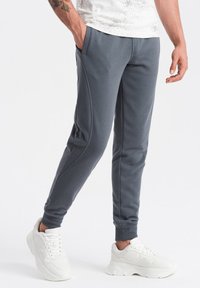 Grå atletiske joggers lavet af blødt stof, med sidelommer og tapered pasform. Parret med hvide sneakers.