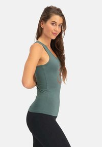 Olivengrünes Tanktop mit einer taillierten Passform, breiten Trägern und einem großen roten Grafikdesign auf der Vorderseite. Der Stoff wirkt glatt und dehnbar.