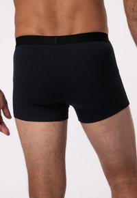 Tmavě modré boxerky vyrobené z měkkého, pružného materiálu. Mají černý pas s embosovaným názvem značky. Přiléhavý střih a hladký povrch.