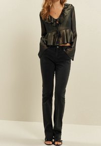 Schwarze ausgestellte Jeans kombiniert mit einem dunklen, schimmernden Peplum-Top mit einem gerafften Ausschnitt und Kordelzug-Detail, abgerundet mit Riemchensandalen.
