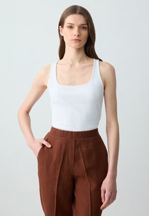 Weißes geripptes Tanktop mit quadratischem Ausschnitt, kombiniert mit hochtaillierten braunen Leinenhosen, die Falten vorne und Eingrifftaschen haben.