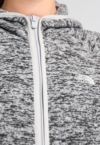 Primo piano di una felpa con zip grigia e nera a mélange, con una zip bianca e il logo The North Face sul petto.