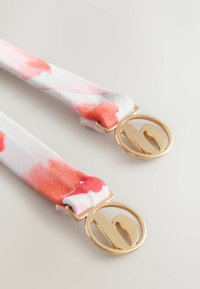 Roosade ja valgete lillemustriliste kangaste rihmad kuldse ringikujulise riistvaraga, millel on stiliseeritud tähemärgiga logo. Sile tekstuur, kerge disain.