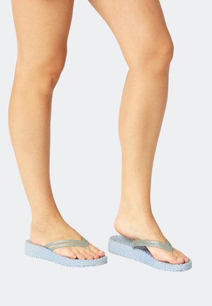 Legs wearing light blue platform flip-flops with glittery silver straps, one foot flat and one heel lifted against a plain background.