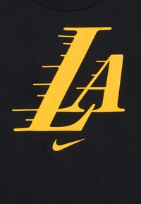 Czarny t-shirt z dużym żółtym napisem "LA" z dynamicznymi liniami przepływu oraz małym białym logo Nike u dołu.