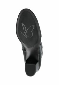 Suela de zapato de goma negra con un patrón texturizado; presenta un logo de mariposa. El tacón es cuadrado y la forma general es ligeramente redondeada.