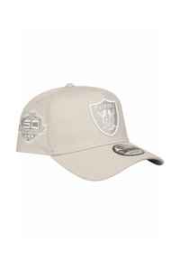 Beige Baseballcap mit gebogenem Schirm, ausgestattet mit weißen gestickten Logos, darunter das Raiders-Schild und ein Gedenkpatch.